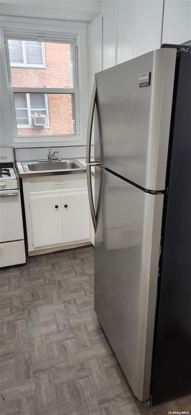 kitchen featuring stainless steel refrigerator, white cabinetry, sink, white range oven, and light parquet flooring