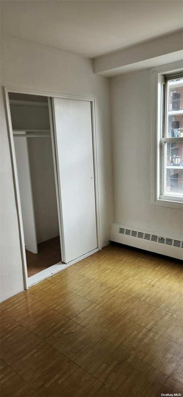 unfurnished bedroom with a closet, baseboard heating, and hardwood / wood-style flooring