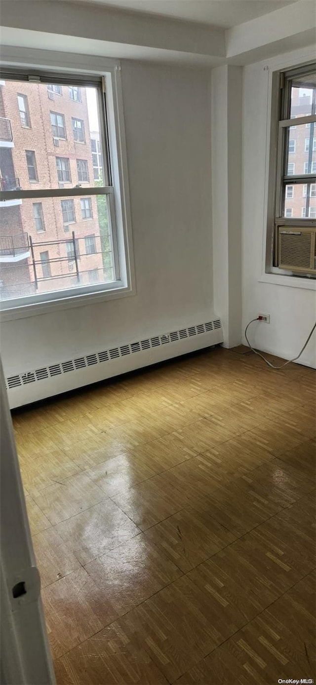 empty room featuring cooling unit, wood-type flooring, and a baseboard heating unit