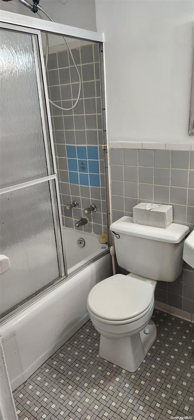 bathroom with tile patterned floors, toilet, enclosed tub / shower combo, and tile walls