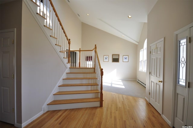 foyer entrance with a baseboard radiator, high vaulted ceiling, plenty of natural light, and light hardwood / wood-style flooring