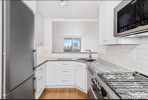 kitchen with light wood-type flooring, premium appliances, sink, stone counters, and white cabinets