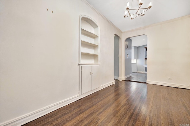 spare room featuring built in shelves, crown molding, dark wood-type flooring, and an inviting chandelier