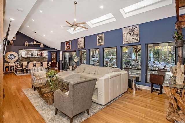 living room with a skylight, high vaulted ceiling, light hardwood / wood-style flooring, and ceiling fan