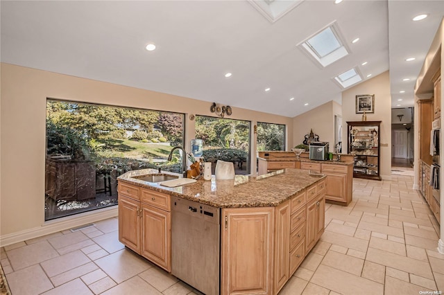 kitchen with dishwasher, lofted ceiling with skylight, light stone countertops, an island with sink, and light brown cabinetry