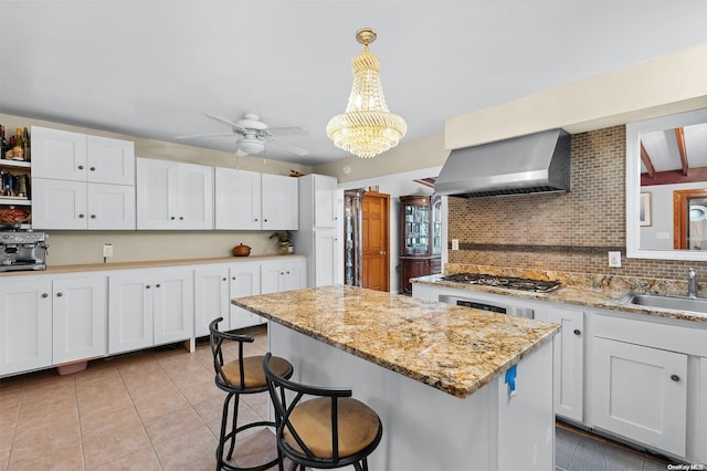 kitchen featuring stainless steel gas stovetop, wall chimney exhaust hood, white cabinets, and decorative light fixtures