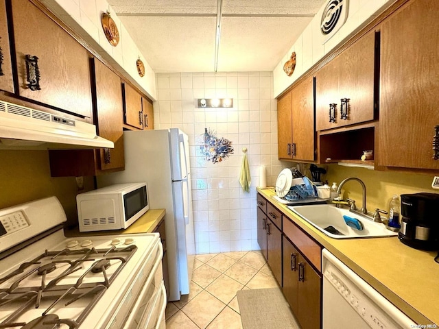 kitchen with light tile patterned flooring, sink, tile walls, white appliances, and a textured ceiling