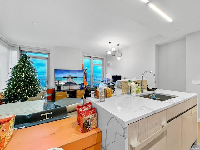 kitchen with light brown cabinetry, sink, hanging light fixtures, and an island with sink