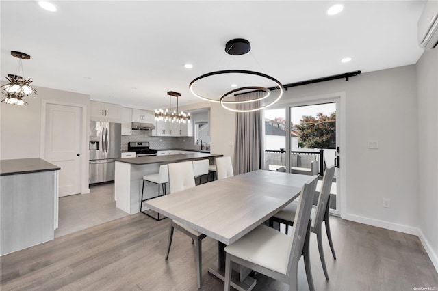 dining space featuring a chandelier, sink, light hardwood / wood-style floors, and a wall mounted air conditioner