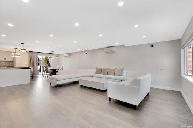 living room with a wall unit AC, light hardwood / wood-style floors, and an inviting chandelier