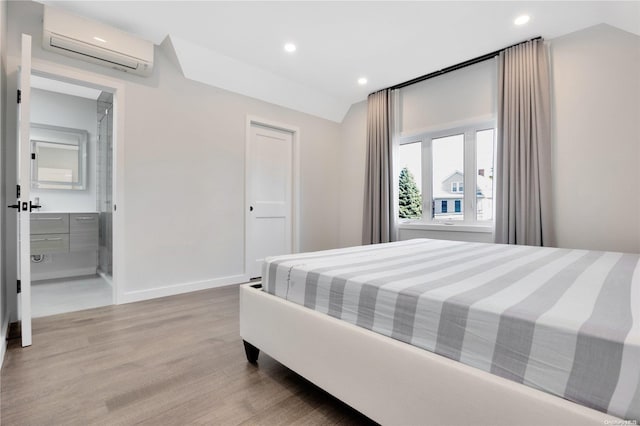 bedroom with hardwood / wood-style floors, ensuite bathroom, and a wall mounted air conditioner