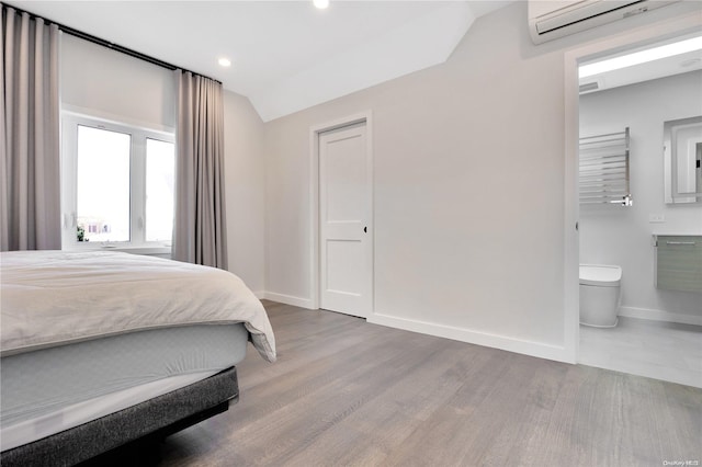 bedroom featuring wood-type flooring, lofted ceiling, an AC wall unit, and ensuite bath