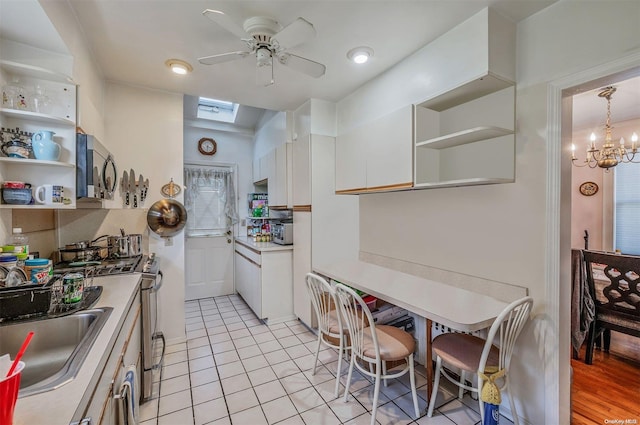 kitchen with appliances with stainless steel finishes, a skylight, ceiling fan with notable chandelier, light hardwood / wood-style flooring, and white cabinetry