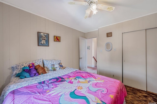 carpeted bedroom featuring ceiling fan, crown molding, wooden walls, and a closet