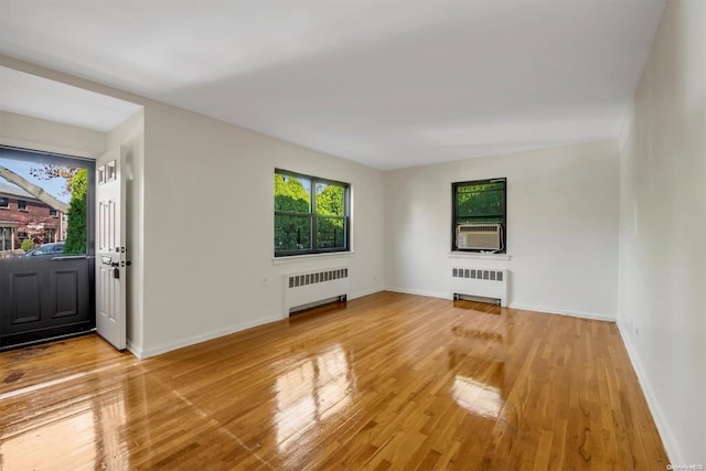 unfurnished living room with radiator heating unit, light hardwood / wood-style floors, and cooling unit