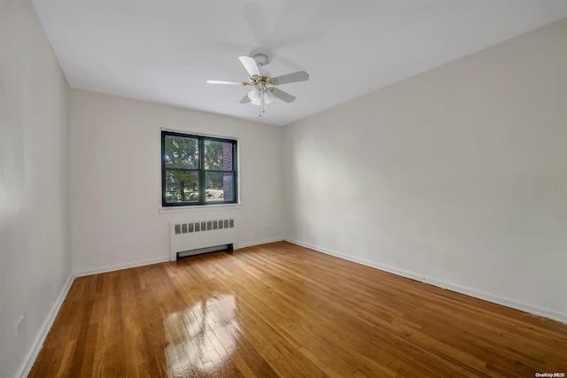 empty room with hardwood / wood-style floors, radiator, and ceiling fan