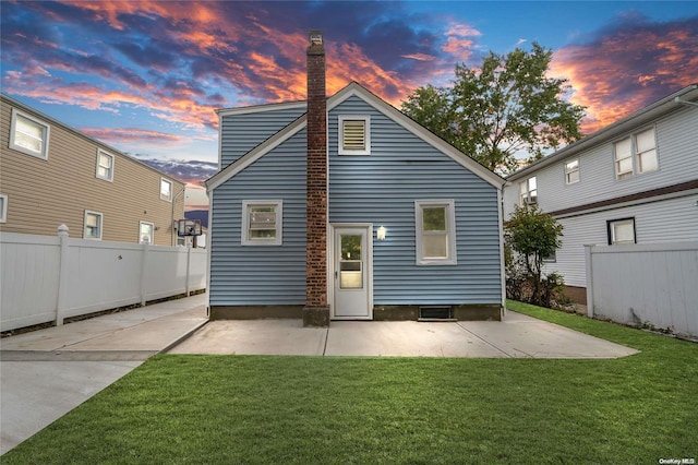 back house at dusk featuring a lawn and a patio area