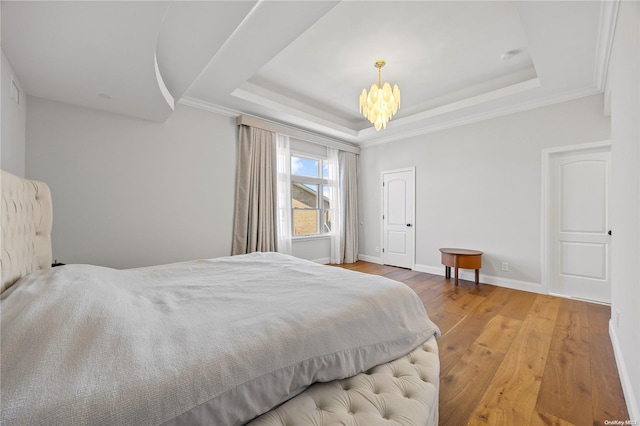 bedroom with a tray ceiling, an inviting chandelier, wood-type flooring, and ornamental molding