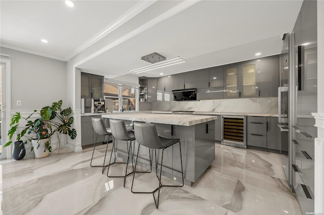 kitchen featuring gray cabinetry, wine cooler, a spacious island, a breakfast bar, and ornamental molding