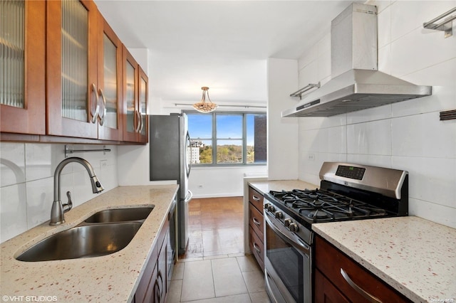 kitchen featuring light stone countertops, wall chimney exhaust hood, stainless steel appliances, sink, and light tile patterned flooring