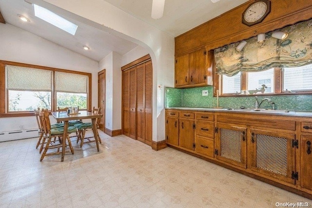 kitchen featuring ceiling fan, sink, tasteful backsplash, a baseboard heating unit, and vaulted ceiling with skylight