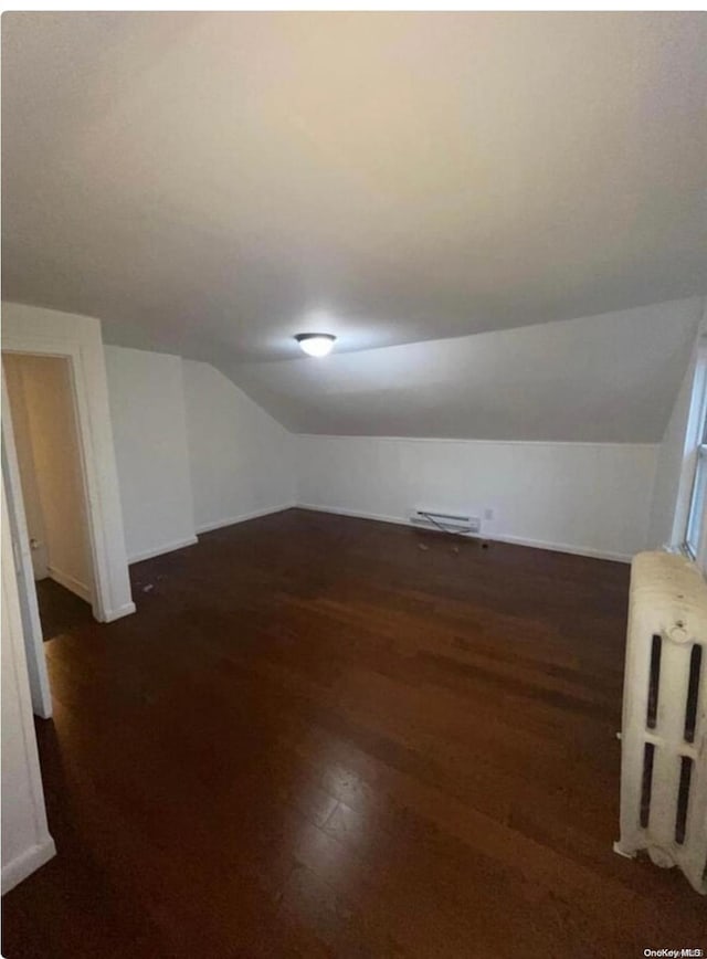 additional living space with radiator, dark hardwood / wood-style flooring, and lofted ceiling