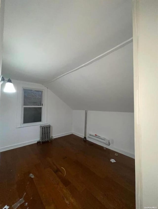 additional living space with dark hardwood / wood-style flooring, vaulted ceiling, and radiator