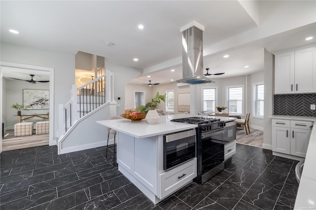 kitchen featuring white cabinets, decorative backsplash, a kitchen island, island range hood, and appliances with stainless steel finishes