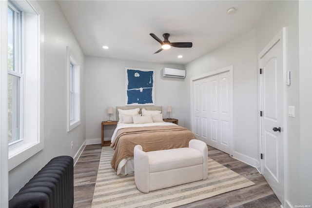 bedroom featuring a wall unit AC, multiple windows, ceiling fan, and hardwood / wood-style flooring