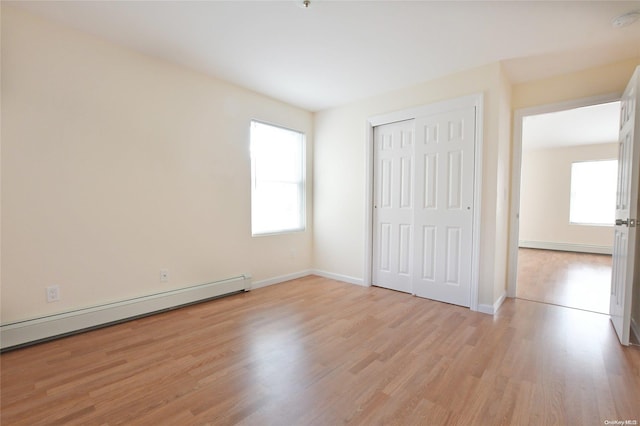 unfurnished bedroom featuring a closet, light hardwood / wood-style flooring, and a baseboard heating unit