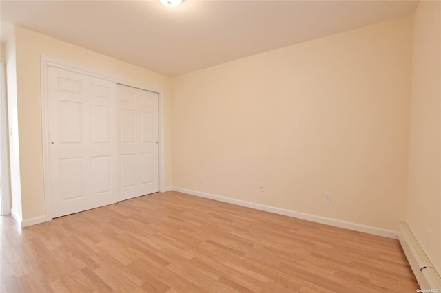 unfurnished bedroom with light hardwood / wood-style flooring, a closet, and a baseboard heating unit