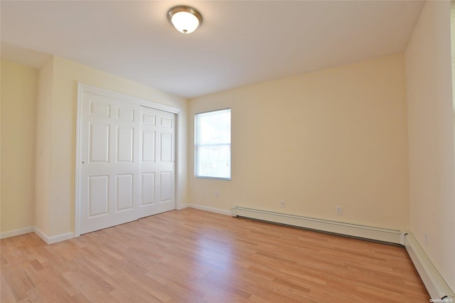 unfurnished bedroom featuring a closet, light wood-type flooring, and a baseboard heating unit