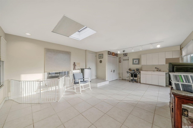 kitchen featuring a skylight, sink, light tile patterned floors, track lighting, and white cabinets