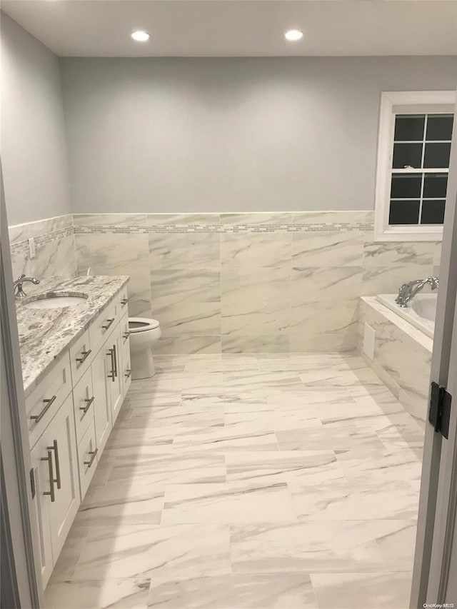 bathroom with vanity, tiled bath, toilet, and tile walls