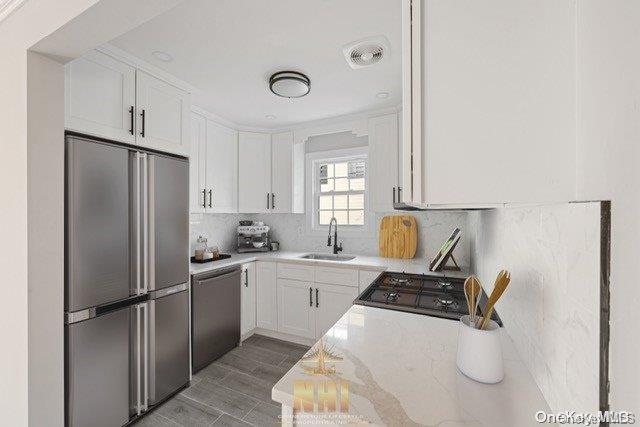 kitchen featuring backsplash, white cabinets, sink, light stone countertops, and stainless steel appliances