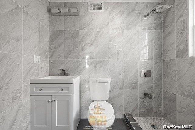 bathroom featuring vanity, toilet, tile walls, and a tile shower