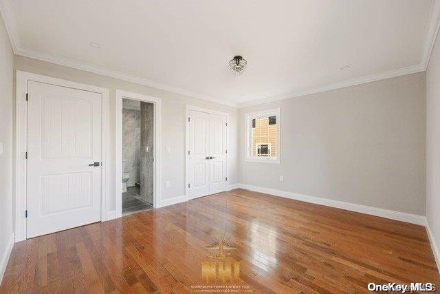 unfurnished bedroom featuring hardwood / wood-style floors, connected bathroom, and crown molding