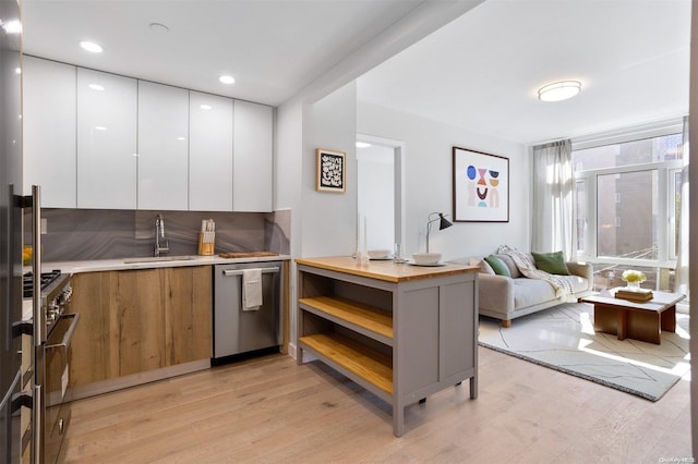 kitchen with kitchen peninsula, light wood-type flooring, stainless steel appliances, sink, and white cabinetry