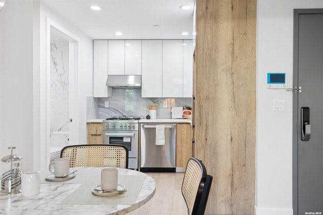 kitchen featuring tasteful backsplash, ventilation hood, white cabinets, and appliances with stainless steel finishes