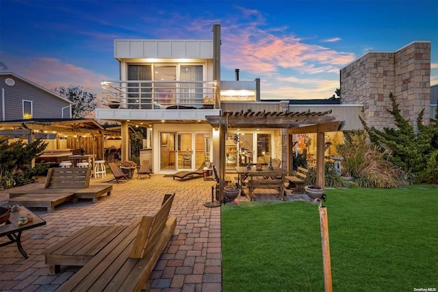 back house at dusk featuring a balcony, a pergola, a patio, and a yard