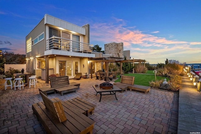 back house at dusk featuring a patio area, a balcony, and an outdoor living space with a fire pit