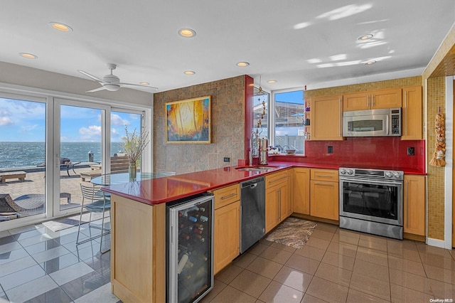 kitchen featuring kitchen peninsula, stainless steel appliances, beverage cooler, sink, and a water view