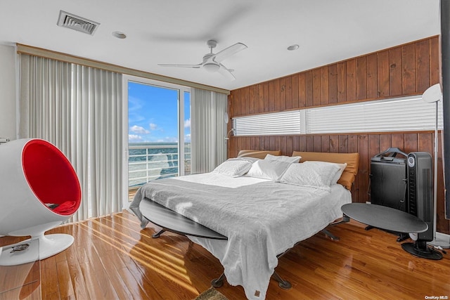 bedroom with hardwood / wood-style flooring, ceiling fan, and wood walls