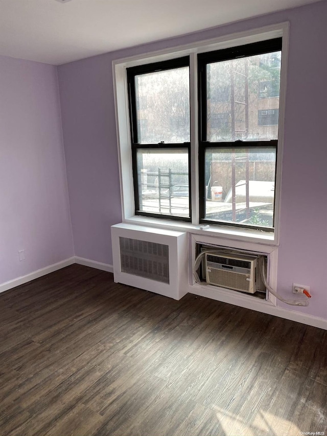 unfurnished room with radiator heating unit, dark wood-type flooring, a wealth of natural light, and a wall mounted AC