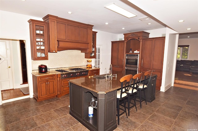 kitchen with dark stone counters, stainless steel appliances, sink, a breakfast bar area, and an island with sink