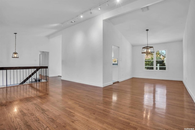 unfurnished living room featuring a notable chandelier, rail lighting, lofted ceiling, and hardwood / wood-style flooring