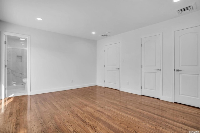 unfurnished bedroom featuring ensuite bath and hardwood / wood-style flooring