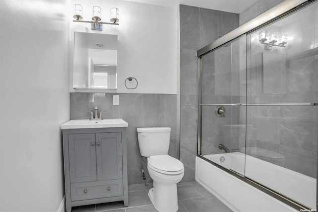 full bathroom with tile patterned floors, vanity, tile walls, enclosed tub / shower combo, and toilet