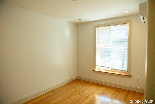 empty room with light wood-type flooring, a wall unit AC, and a wealth of natural light