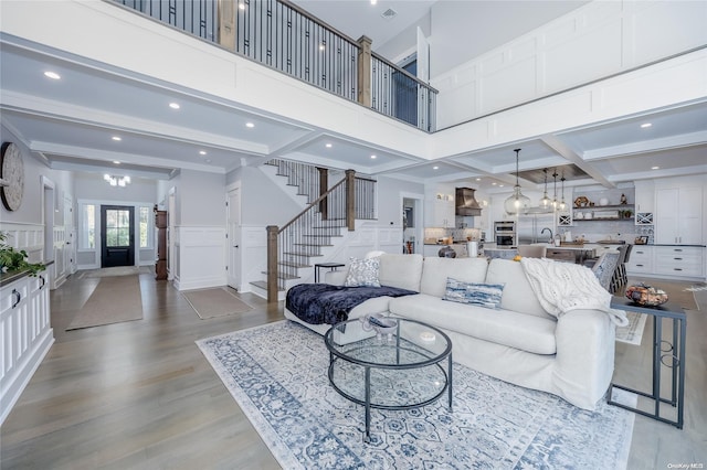 living room featuring sink, coffered ceiling, beamed ceiling, a towering ceiling, and light hardwood / wood-style floors